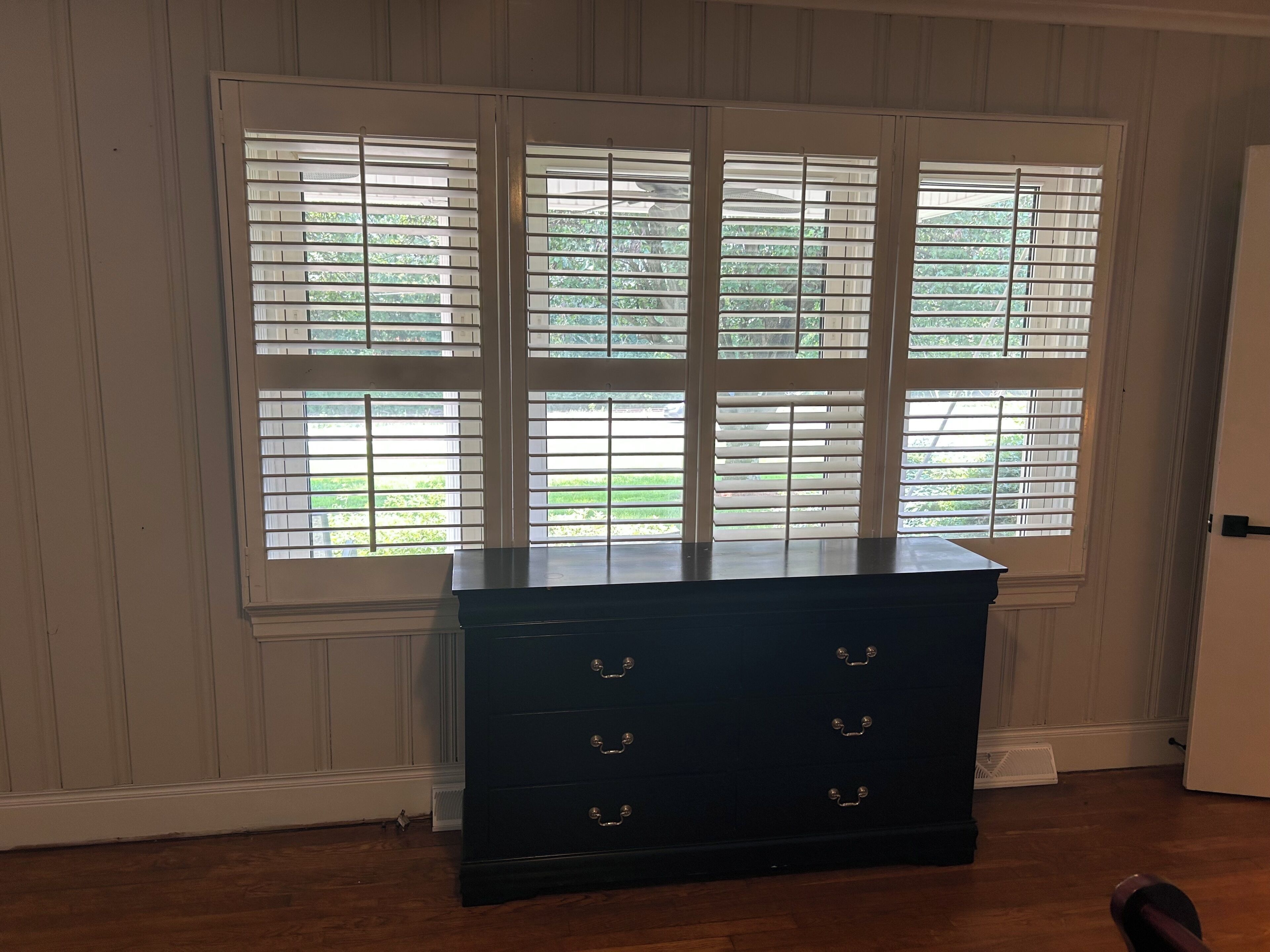 A room with a dark wooden dresser against a wall with white paneled trim.
