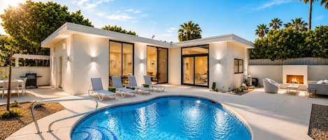 A modern house with a swimming pool, outdoor seating, and a fireplace.