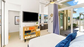 Quarto moderno com uma cama grande, televisão, cómoda de madeira e porta de vidro deslizante para uma varanda.