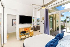 Ein modernes Schlafzimmer mit einem großen Bett, einem Fernseher, einer hölzernen Kommode und einer Glastür zum Balkon.