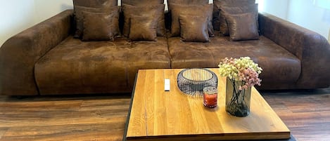 Un canapé en cuir marron agrémenté de plusieurs coussins, une table basse en bois sur laquelle est posé un vase de fleurs, et un tableau représentant un champ parsemé de fleurs rouges, accroché au mur.