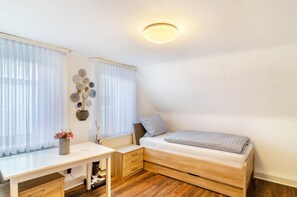 Un dormitorio pequeño y ordenado con cama, escritorio y radiador.