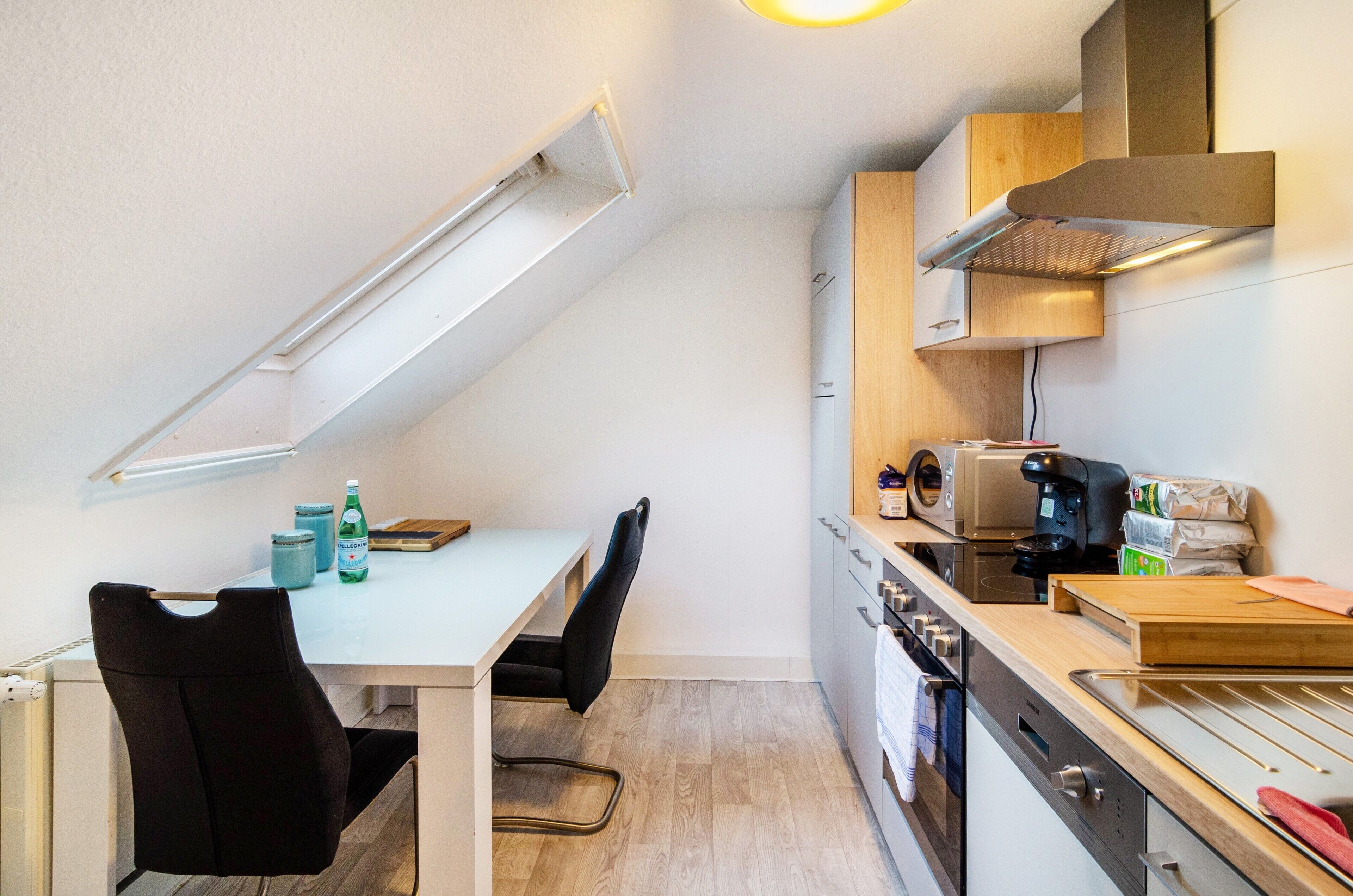 Et kompakt køkken med spisebord, stole, mikroovn og komfur.