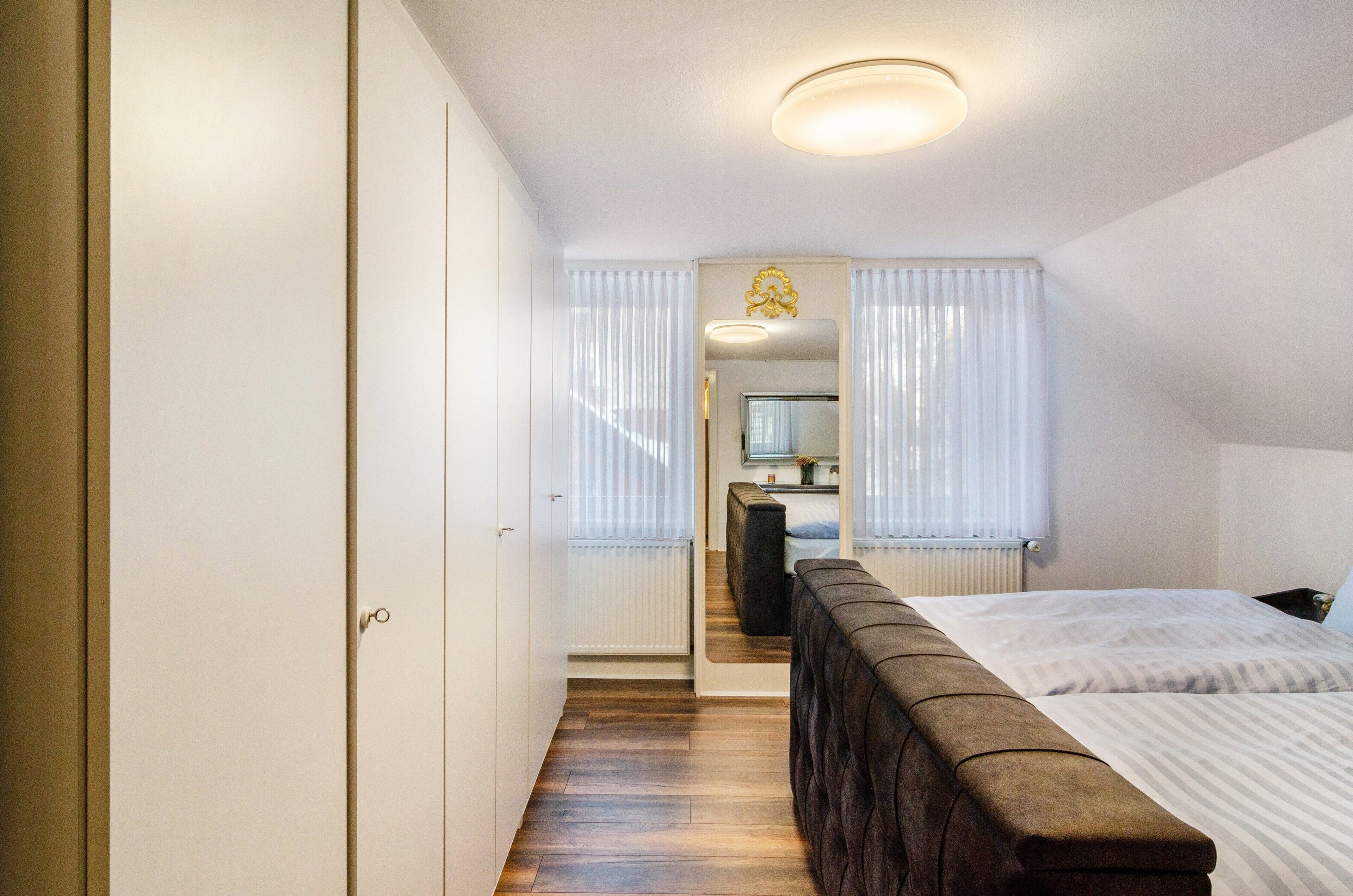 Une chambre à coucher avec un lit, un banc en bois, une armoire et une salle de bain visible à travers une porte.