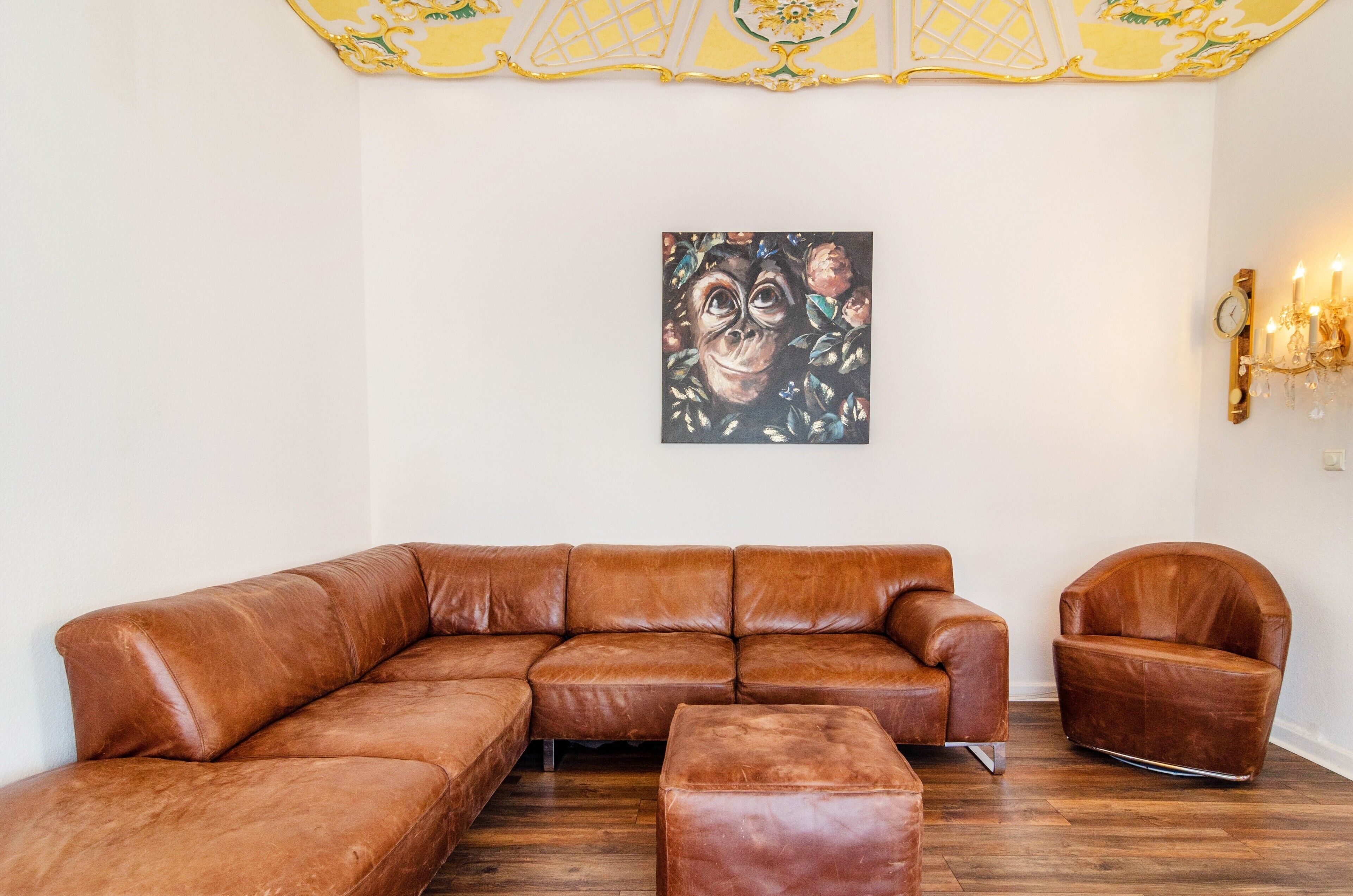 Ein braunes, ledernes Ecksofa, ein passendes Ottomanen und ein brauner Ledersessel in einem Raum mit Holzboden und einer dekorativen Decke.