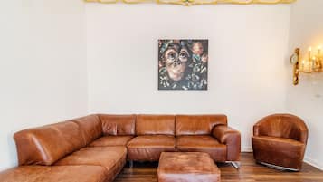 Ein braunes, ledernes Ecksofa, ein passendes Ottomanen und ein brauner Ledersessel in einem Raum mit Holzboden und einer dekorativen Decke.