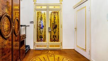 Ein Zimmer mit Holzboden, einer weißen Tür mit Goldverzierungen und einem großen Spiegel mit aufwendiger Holzvertäfelung.