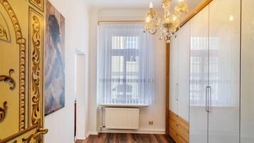Ein Zimmer mit Heizkörper, einem Fenster mit durchsichtigen Vorhängen, einer Chandelierleuchtreiter und einer Tür mit aufwendiger Gestaltung.