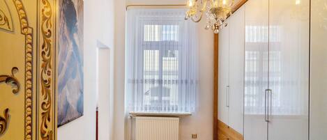 A room with a radiator, a window with sheer curtains, a chandelier, and a door with ornate design.