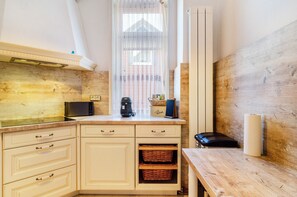Una cocina con armarios de madera, microondas, cafetera y una ventana con cortinas traslúcidas.