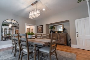 A dining area with a wooden table and chairs, a chandelier, a mirror, and a cabinet with decorative items.