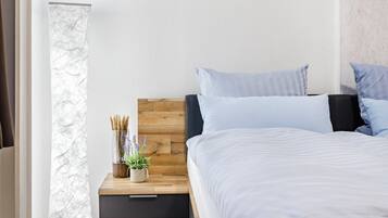 Ein Schlafzimmer mit einem hölzernen Kopfteil, einem Nachttisch mit Pflanze und einem Bett mit weißer Bettwäsche.