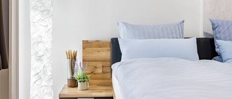 A bedroom with a wooden headboard, a bedside table with a plant, and a bed with white bedding.