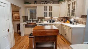 Une cuisine avec des meubles blancs, un îlot central en bois et une fenêtre au-dessus de l’évier.