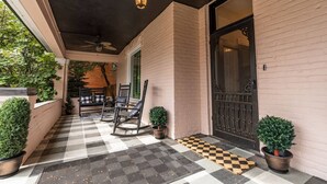 Une véranda couverte avec un sol à carreaux, deux fauteuils à bascule et des plantes en pot.