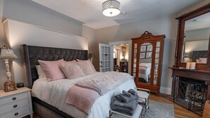 Een slaapkamer met een groot bed, nachtkastjes, een spiegel en een open haard.