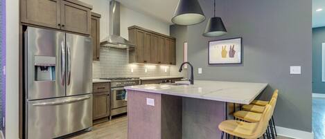 A modern kitchen with stainless steel appliances, wooden cabinets, and a central island with bar stools.