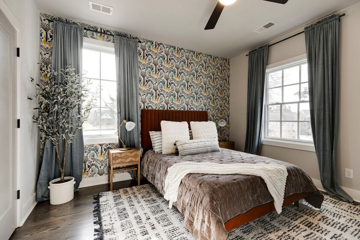 Quarto com cama grande, mesa de cabeceira, planta em vaso e janela com cortinas.