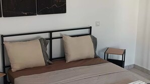 Seng med gavl, puder og dyne. Et lille bord og en stol står ved siden af sengen.