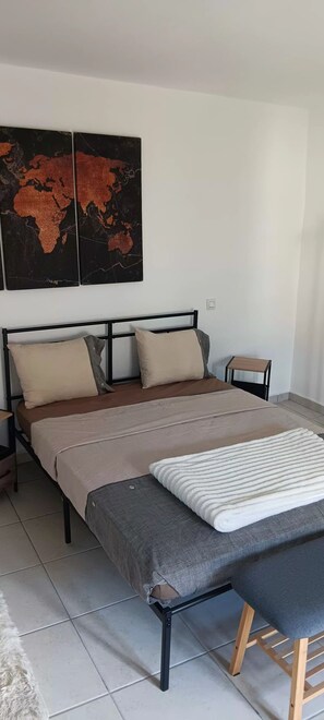 Ein Bett mit Kopfteil, Kissen und Decke. Ein kleiner Tisch und ein Stuhl stehen daneben.