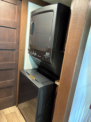 A compact washer and dryer unit with a control panel, situated in a narrow space with wooden doors. - Peaceful tiny home in cozy mentone (Mentone)