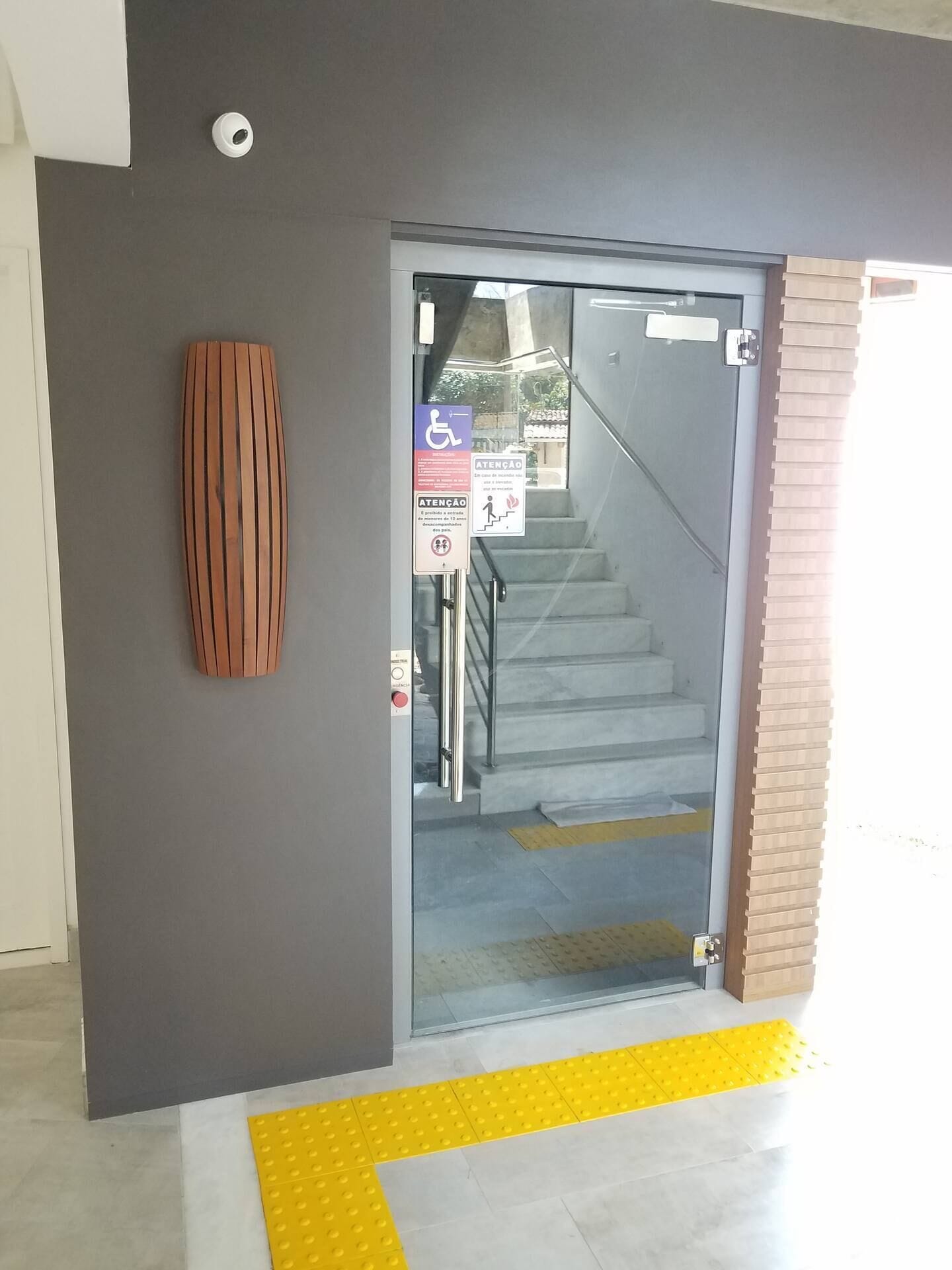 Une entrée moderne, dotée d’une porte en verre, d’une rampe et d’une bande de revêtement tactile pour les personnes malvoyantes.