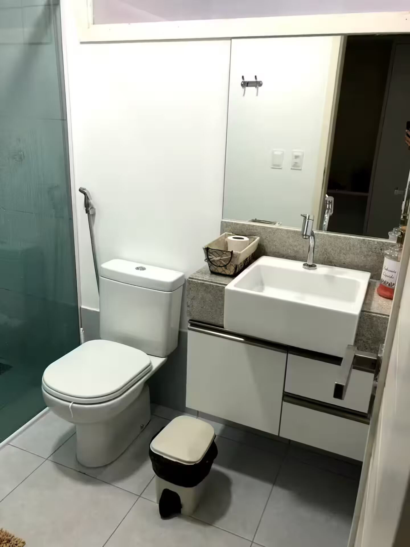 Uma casa de banho compacta com sanita, bidé, lavatório e armário de arrumação.