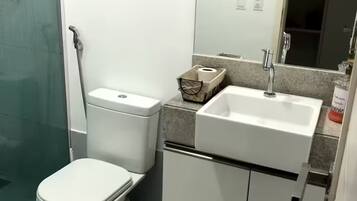 Uma casa de banho compacta com sanita, bidé, lavatório e armário de arrumação.