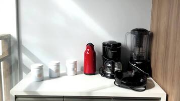 Un comptoir de cuisine avec une machine à café, une bouteille d’eau rouge et un mixeur.