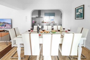 Een eetgedeelte met een tafel gedekt voor zes personen, een keuken op de achtergrond en een ingelijste foto aan de muur.