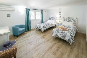 Une chambre avec deux lits simples, un bureau, une chaise et un fauteuil en osier.