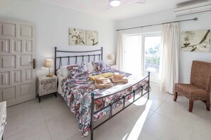 Ein Schlafzimmer mit einem Bett, einem Sessel, einem Nachttisch und einem Fenster mit Vorhängen.