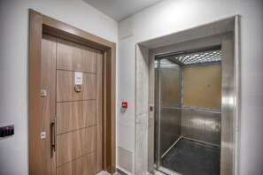 Ein Aufzug mit metallischem Innenraum und einer Holztür mit Schloss und Beschriftung.