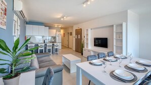 Een modern appartement met een eethoek, keuken, woonkamer en een aan de muur bevestigde televisie.