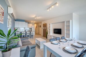 A modern apartment with a dining area, kitchen, living room, and a TV mounted on the wall. - Modern Qawra Apartment with Sea View (St. Paul`s Bay)