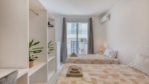 Een hotelkamer met twee bedden, een bloempot, een balkon met een hekwerk en een airconditioning.