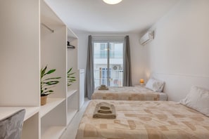 A hotel room with two beds, a potted plant, a balcony with a railing, and an air conditioning unit. - Modern Qawra Apartment with Sea View (St. Paul`s Bay)