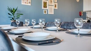 Een eettafel gedekt met borden, bestek en wijnglazen, met een plant en ingelijste foto's aan de muur.
