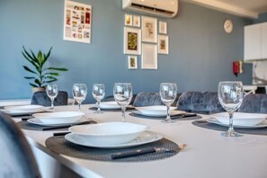 A dining table set with plates, cutlery, and wine glasses, with a plant and framed pictures on the wall. - Modern Qawra Apartment with Sea View (St. Paul`s Bay)