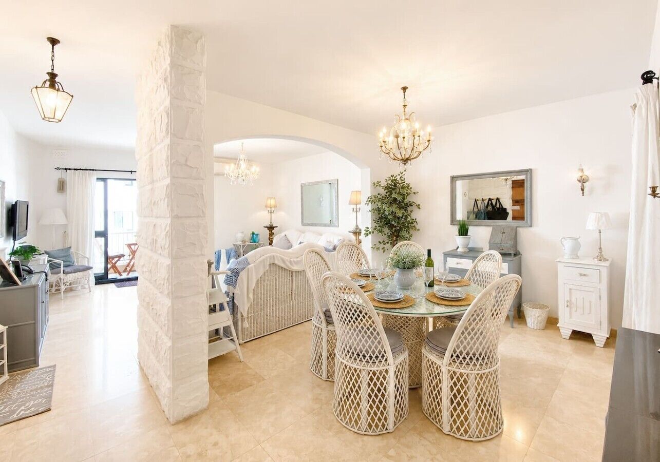 A dining area with wicker chairs, a glass table, and a chandelier.