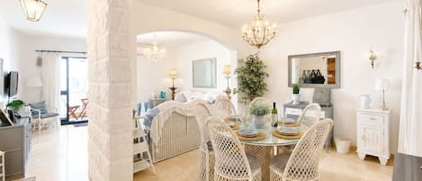 A dining area with wicker chairs, a glass table, and a chandelier.