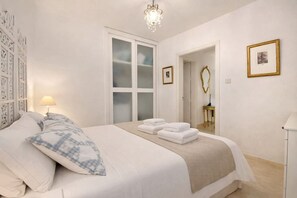 Habitació d'hotel amb llit, una tauleta de nit, una làmpada, un mirall i una porta que dona a una altra habitació.