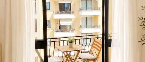 Un balcone con tavolo e sedie, vista su un edificio con balconi e tende leggere.