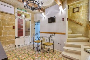 A room with a patterned floor, a chair, a table, a staircase, and a fire exit sign. - Charm Suite Valletta (Valletta)
