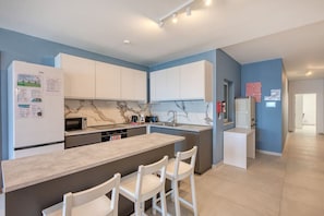 Een moderne keuken met witte kastjes, een marmeren spatwand en een centraal eiland met barstoelen.