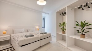 A modern bedroom with a bed, bedside tables, a hanging light fixture, and two potted plants. - Modern Apartment with Sea View Qawra (St. Paul`s Bay)
