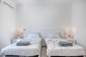 A twin room with two beds, each with a nightstand, a lamp, and a folded towel. - Modern Apartment with Sea View Qawra (St. Paul`s Bay)
