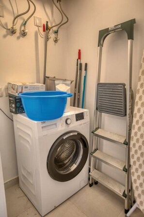 Ein Waschbereich mit Waschmaschine, Wäscheständer und blauem Becken.