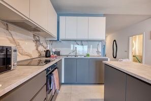 A modern kitchen with a built-in oven, microwave, and a large island with a sink. - Modern Apartment with Sea View Qawra (St. Paul`s Bay)
