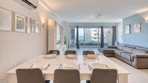 A modern dining area with a table set for four, a sofa, and a balcony with outdoor seating. - Modern Apartment with Sea View Qawra (St. Paul`s Bay)